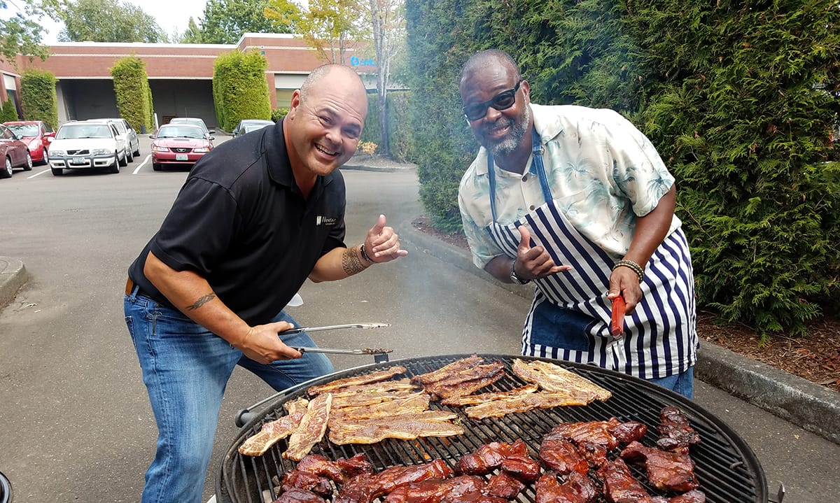 Two Westlake employees smiling in front of a charcoal grill