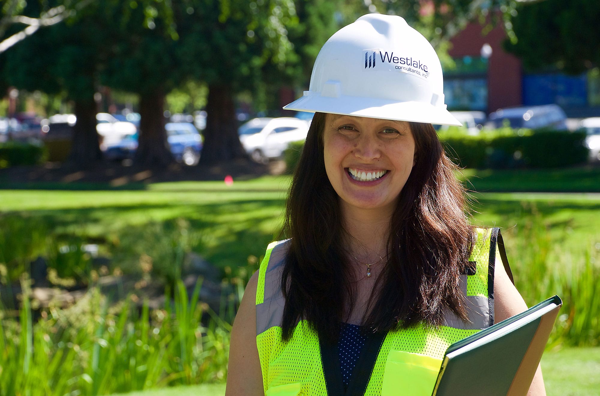 Westlake employee smiling wearing a white hard hat and neon green safety vest